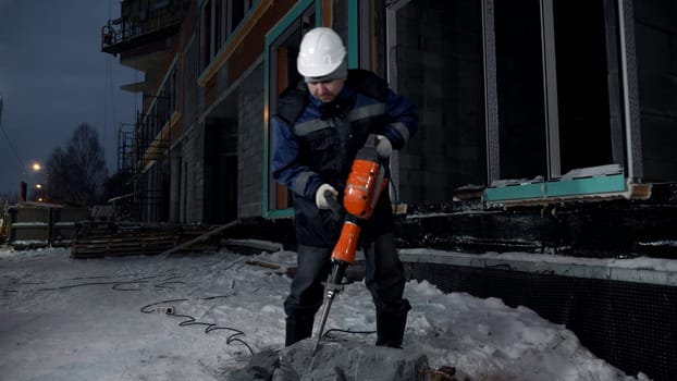 Construction worker uses hydraulic drill at construction site. Clip. Process of crashing a concrete block