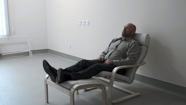 Man is lying in armchair in office. Clip. Man is lying in armchair in empty white room. Man in therapist's chair. Psychological illness.