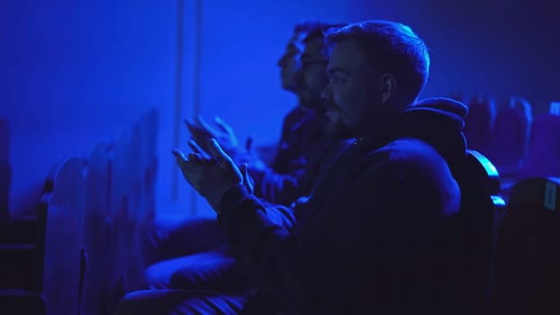 Men applaud performance in theater. Media. Men sit in one row and clap for performance. Theatrical performance with dark hall and applauding audience.