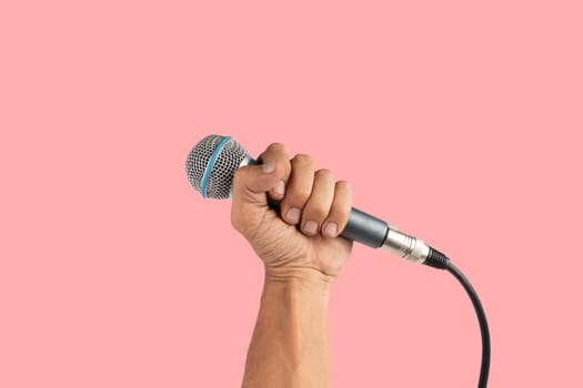 Black male hand holding a microphone isolated on pink background. High quality photo