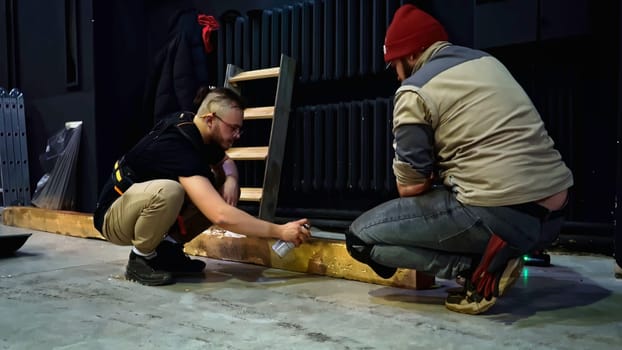 Spray painting of wooden beam in a concert hall. Media. Young man decorating wooden beam by black paint