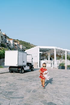 Little girl with a stuffed bunny walks past a cargo golf cart. High quality photo