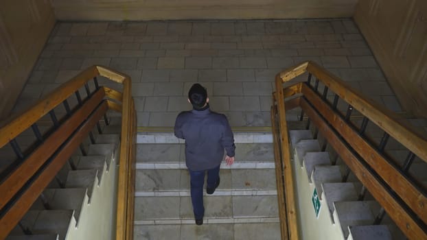 Top view of man walking up stairs of old building. Media. Young man climbs stairs in old university building. Man walks up stairs in theater or university college building.