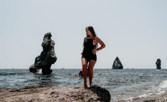 Woman travel sea. Young Happy woman in a long red dress posing on a beach near the sea on background of volcanic rocks, like in Iceland, sharing travel adventure journey