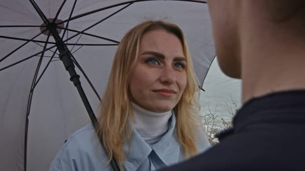 Portrait of a woman with umbrella listening carefully to a man. Stock clip. Romantic couple by the sea on a rainy day