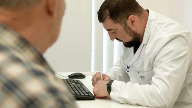 Male doctor working at the table, writing prescription. Clip. Old male patient at the hospital