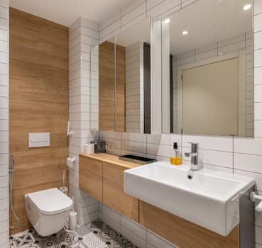 A bright, modern bathroom featuring wooden accents, white tiles, a wall-mounted toilet, and a spacious sink for a stylish and clean look.