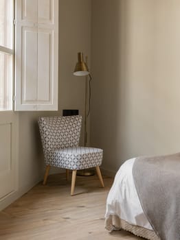 Comfortable and stylish bedroom corner featuring a patterned chair, contemporary floor lamp, and soothing neutral decor. Ideal for home and interior design inspiration.