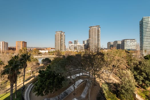 Panoramic view of a city skyline featuring modern high-rise buildings and a green park under a clear blue sky.