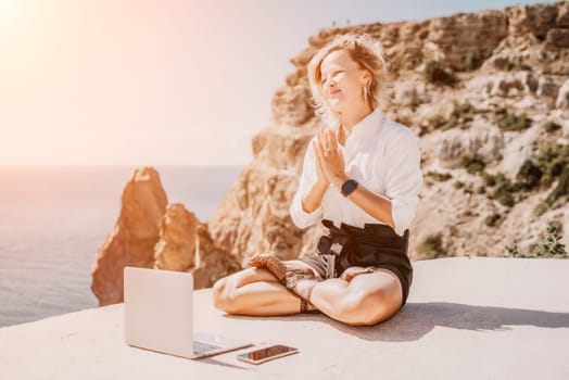 Happy girl doing yoga with laptop working at the beach. beautiful and calm business woman sitting with a laptop in a summer cafe in the lotus position meditating and relaxing. freelance girl remote work beach paradise