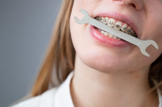 Close-up portrait of a woman with braces holding a wrench in her teeth