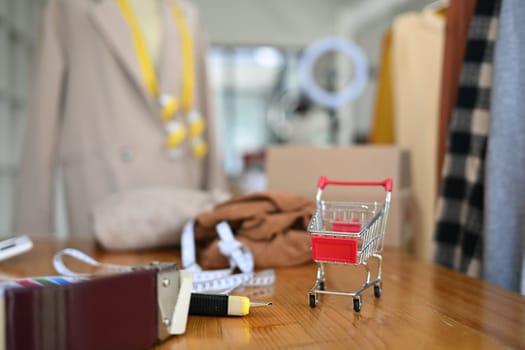 A shopping cart on wooden table at tailors studio. E-commerce, online shopping and small business concept.
