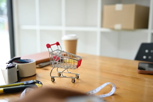 Shopping cart on wooden table in the warehouse. E-commerce, online shopping and small business concept.