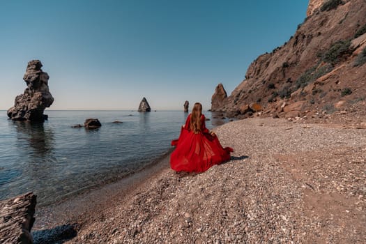 A woman in a red dress stands on a beach with a rocky shoreline in the background. The scene is serene and peaceful, with the woman's red dress contrasting against the natural elements of the beach