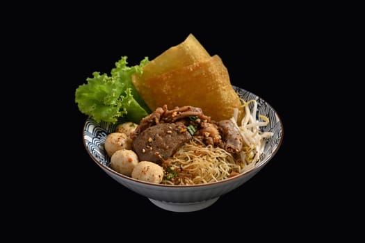 Spicy egg noodles with sliced braised beef, meatballs and vegetables in a bowl on black background. Thai noodle.