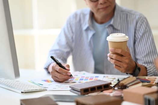 Cropped shot of senior architect with paper cup of coffee sitting in the creative office.