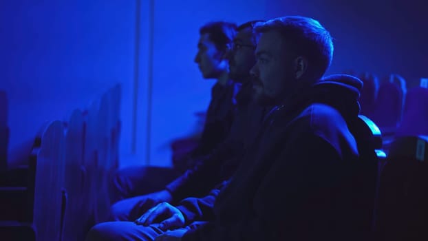 Young men watching movie at cinema. Media. Men were watching movie intently in dark cinema. Men in their seats in cinema.