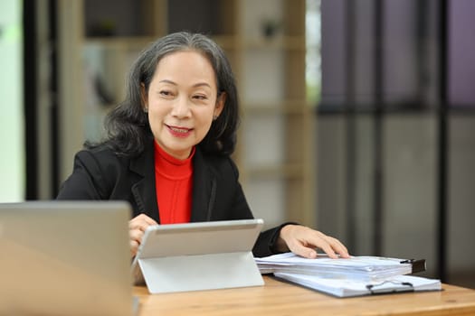 Portrait of smiling mature business woman manager using digital tablet at desk.