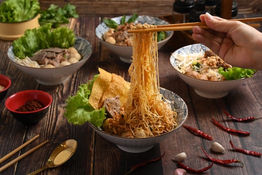 Hand using chopsticks to picking up tasty spicy egg noodles from bowl. Thai noodles and Asian food concept.