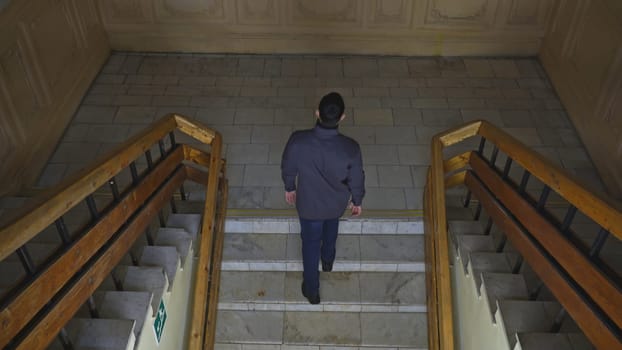 Top view of man walking up stairs of old building. Media. Young man climbs stairs in old university building. Man walks up stairs in theater or university college building.