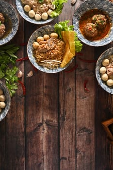 Top view assorted tasty Thai noodles soup, meatballs and dumpling on rustic wooden table. Asian food.