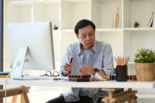 Portrait of senior architect or interior designer working with sample of wooden panel at desk.