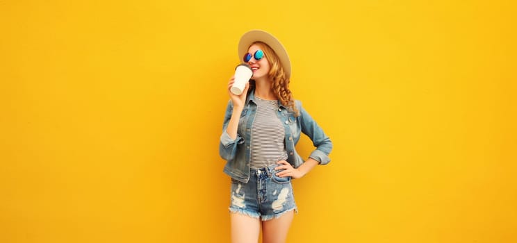 Beautiful stylish happy smiling young woman with cup of coffee wearing summer hat, jean jacket posing on yellow background