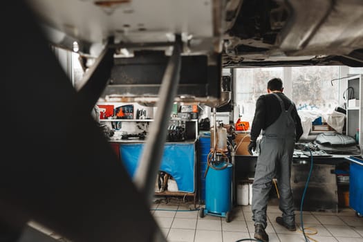 Workman mechanic working under car in auto repair shop close up