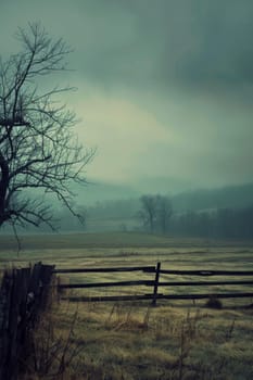 A moody rural landscape shrouded in fog, with a bare tree and a dilapidated fence, evoking the quiet of a late autumn day.