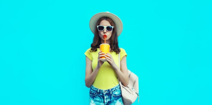 Summer portrait of beautiful caucasian young woman with cup of coffee or fresh juice wearing a straw hat on studio blue background