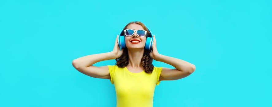 Portrait of happy modern happy young woman listening to music with headphones on blue background