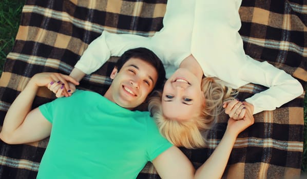 Portrait of beautiful happy smiling young couple in love lying together on a blanket having a picnic, top view, summer park