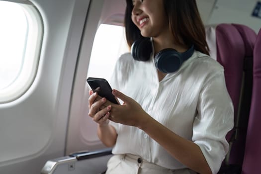 Beautiful Asian in aeroplane. working, travel, business concept Traveler on Plane Using Smartphone with Headphones, Smiling and Happy.