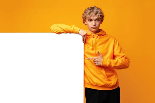 Young man holding a blank panel for advertising against yellow background, copy space