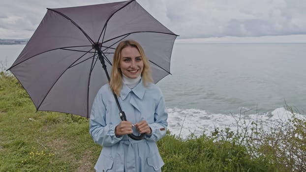 Tender woman with umbrella closing her boyfriend eyes with her hand at the sea shore. Stock clip. Cold windy weather at the sea coast