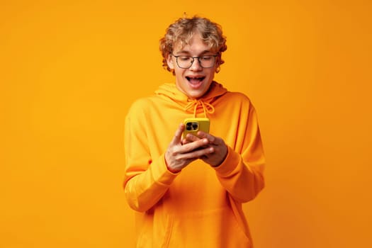 Happy caucasian young man using smartphone against yellow background close up