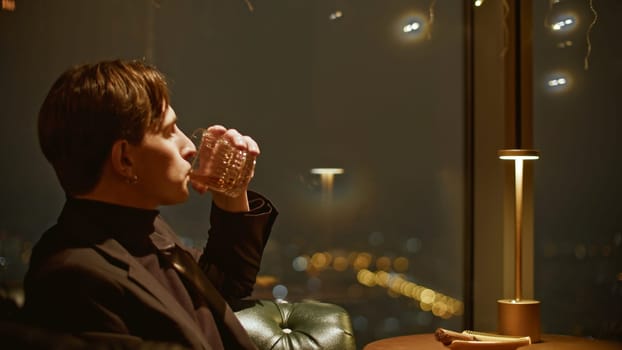 Young attractive man drinks whiskey in restaurant. Media. Young single man in suit drinks scotch in restaurant. Cinematic handsome man in suit at whiskey restaurant.