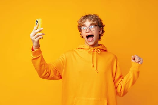 Portrait of young man playing online game on mobile phone over yellow background close up