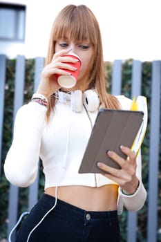 Front view of a caucasian teenage girl laughing using a social media app with her digital tablet, drinking coffee. University Life Concept