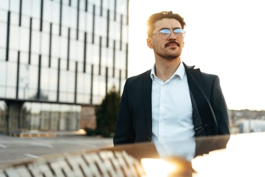 Confident young businessman in suit standing near his car outdoors