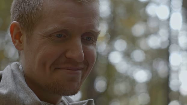 Close-up of man smiling and talking in woods. Stock. Cinematic portrait of man in style of teacher in forest. Man speaks and smiles like sensei.