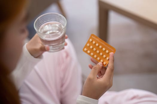 Woman holding birth control pills and a glass of water. Concept of contraception and healthcare routine.