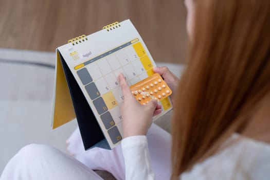 Woman holding birth control pills and checking calendar. Concept of contraception and family planning.