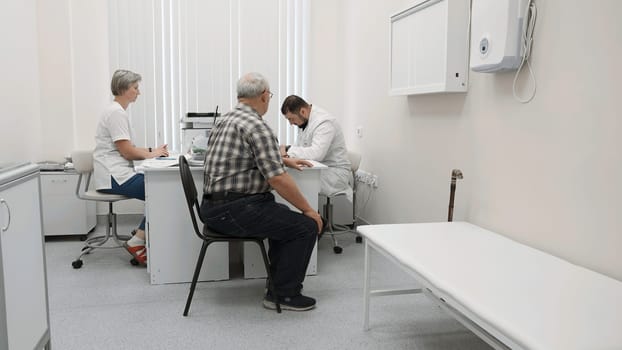 Elderly man in office at doctor's appointment. Clip. Patient at doctor's appointment with nurse in modern clinic. Elderly man complains of ailments at doctor's appointment.