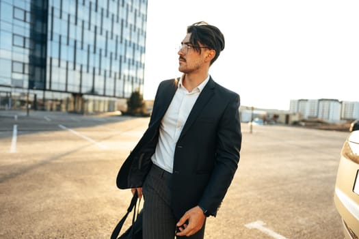 Portrait of confident attractive businessman in suit looking at camera near office building, outdoors