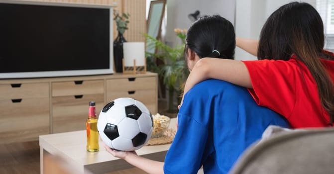 A lesbian couple cheers football and celebrate together for their favorite Euro football team. A young female couple cheers football on TV together in the living room on match day..