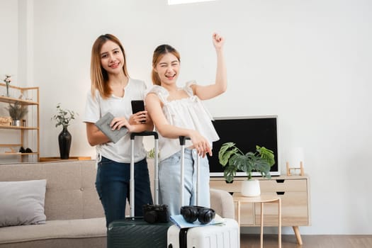 Happy Asian women ready for travel with passports and luggage in living room. Indoor concept of excitement and travel preparation.