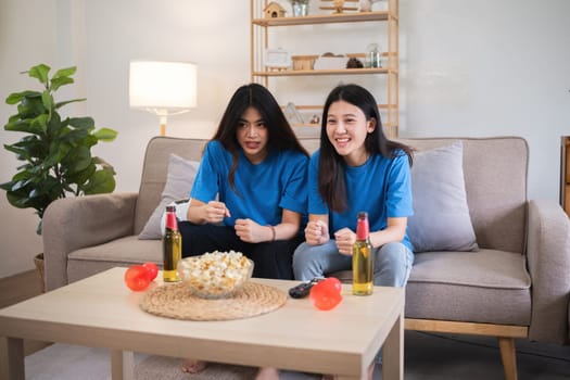 Asian lesbian couple watching a sports game on TV at home. Concept of love, companionship, and enjoying leisure time together in a cozy indoor setting.