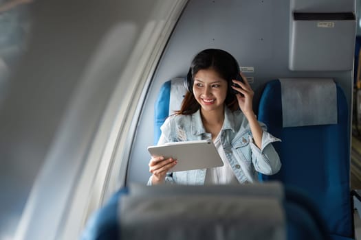 Successful beautiful young asian business woman sit in airplane and work on digital tablet. Flying at first class.