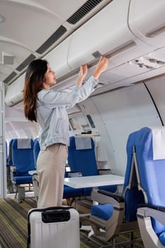 Asian woman storing luggage in airplane overhead bin. Concept of travel, preparation, and aviation.